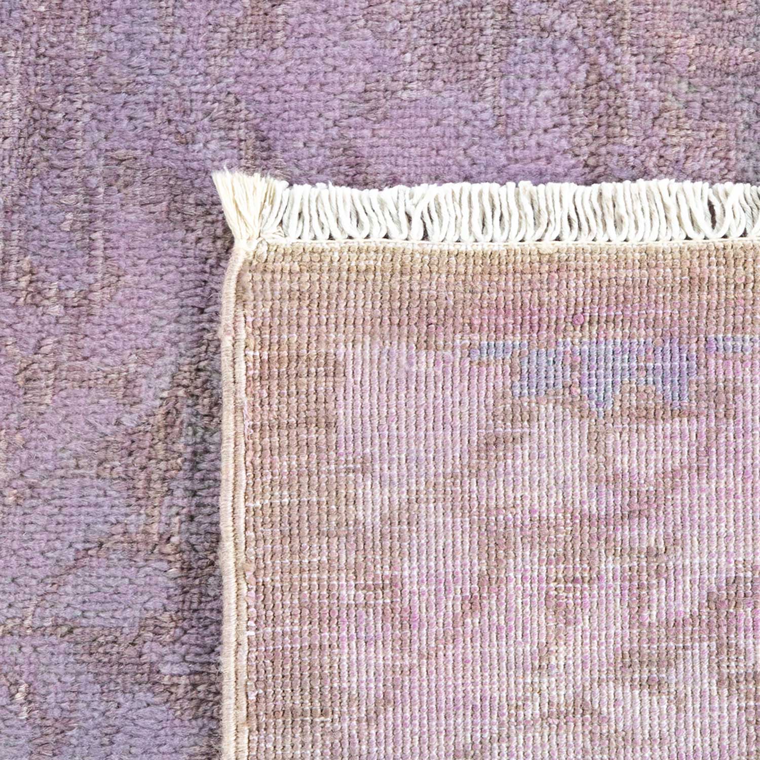 Close-up of two different types of fabric: plush purple carpet and beige fringed textile.