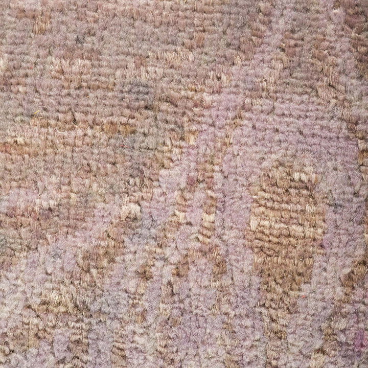 Close-up of a worn, distressed carpet with muted pink tones.