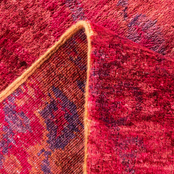 Close-up of vibrant woven textile with rich red hues and intricate patterns, showcasing texture and folded underside with contrasting binding.