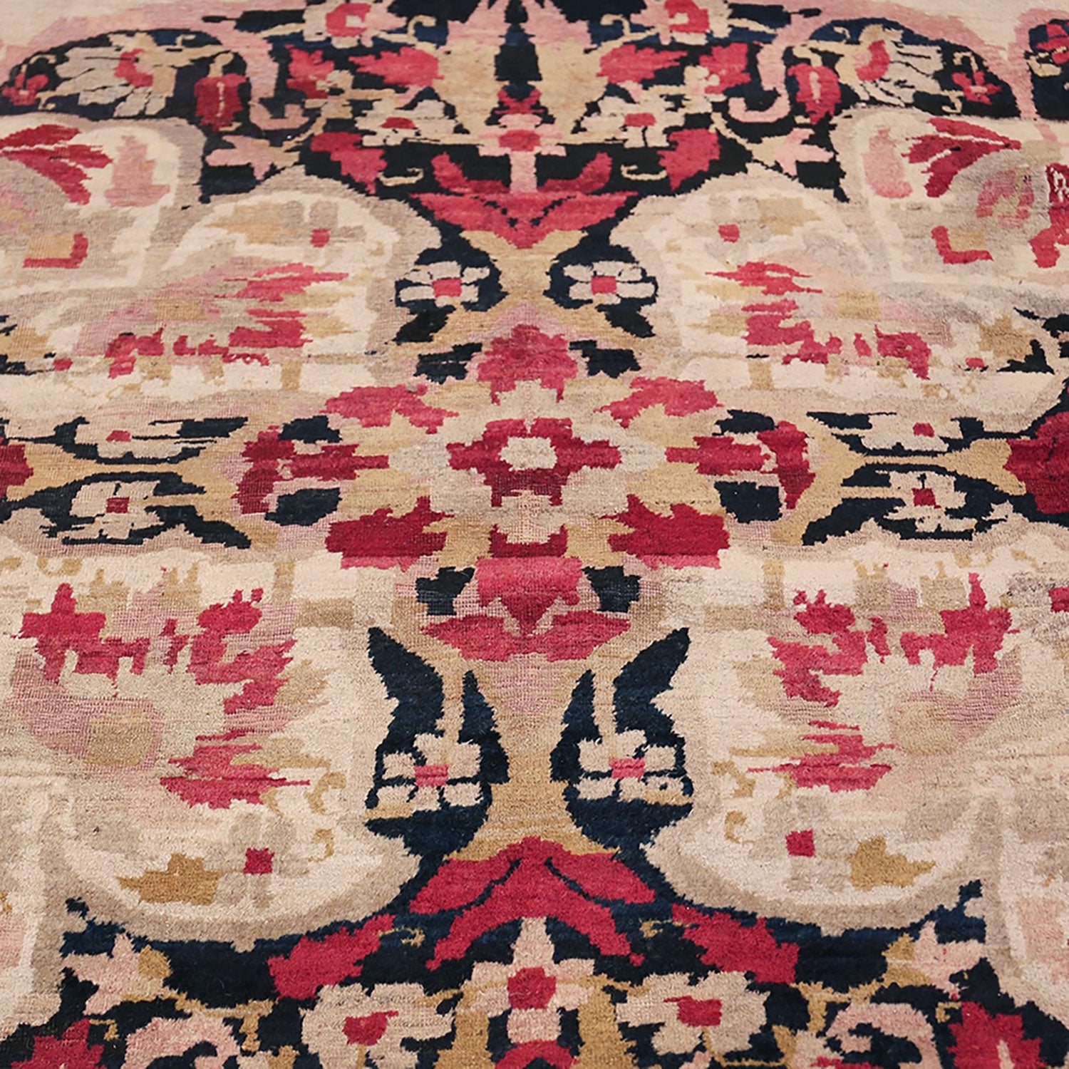 Close-up view of a traditional rug with intricate floral and geometric patterns in shades of red, pink, black, and beige.