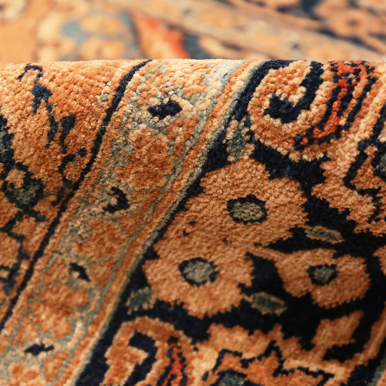 Intricately patterned rolled-up carpet in vibrant orange, beige, and blue.
