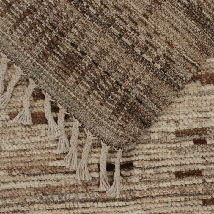 Close-up of handwoven textile with earthy tones and fringed edge.
