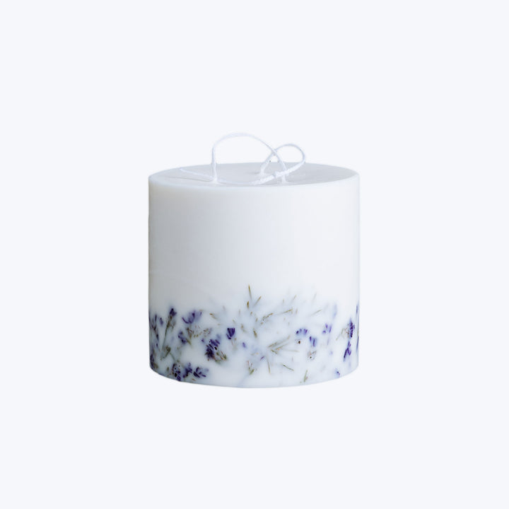 White cylindrical candle with dried lavender flowers, unused wick.