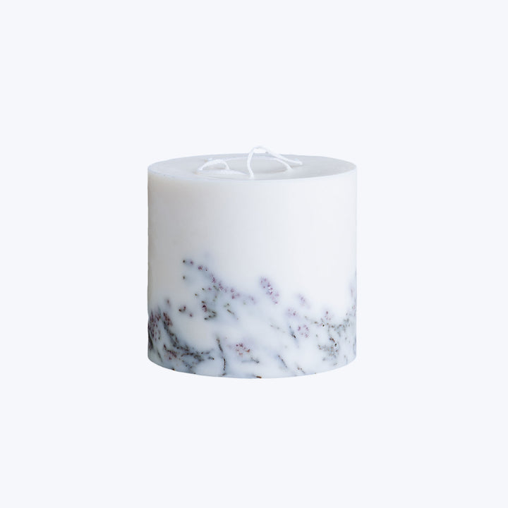 Marbled cylindrical candle with dried herbs and two wicks, unlit.