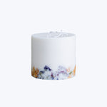 Botanical-infused white candle with unlit wick, purple and orange hues.