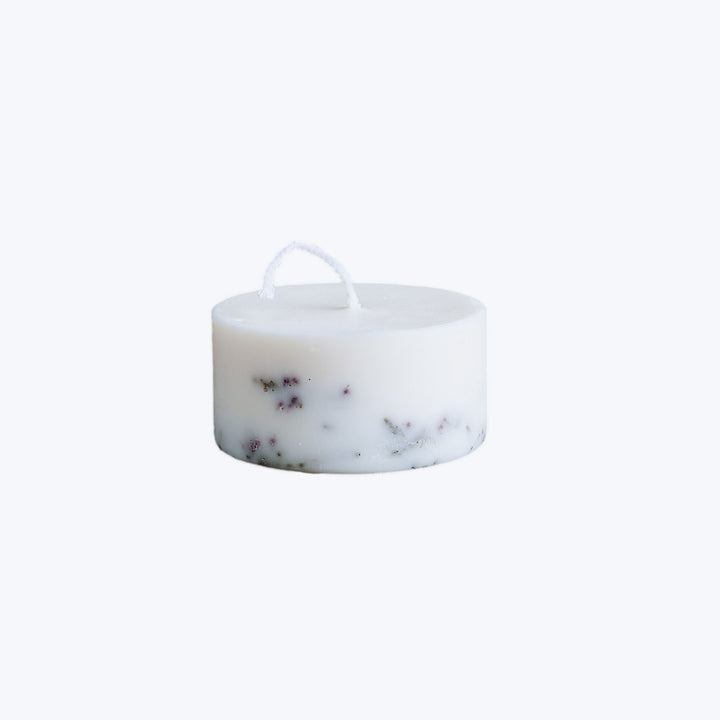 Decorative white candle with scattered herbs on white background.