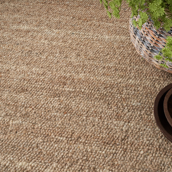 Close-up of neutral loop pile carpet with greenery and wood.