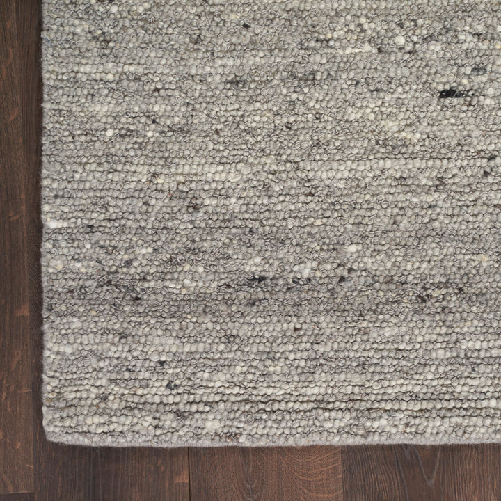 Close-up view of grey textured carpet on dark wood floor.