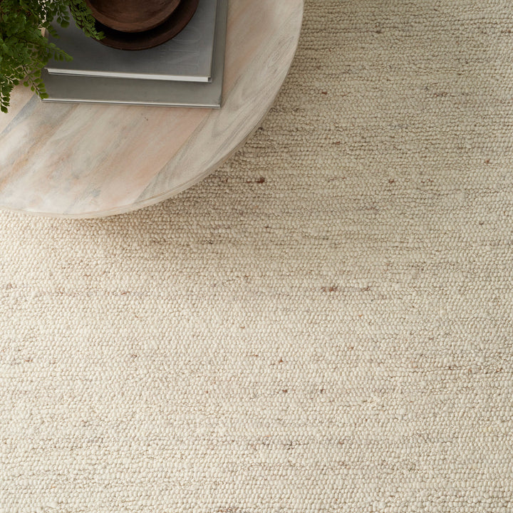 Close-up of cream carpet with wooden table, plant, and vase.