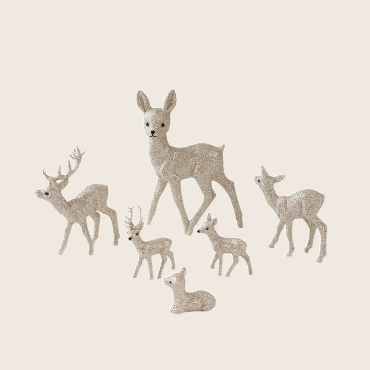 Seven glittery deer figurines in various sizes and poses. Festive decor.