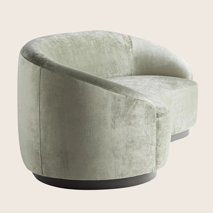 Modern armchair with rounded shape and velvet upholstery in pale green or gray.