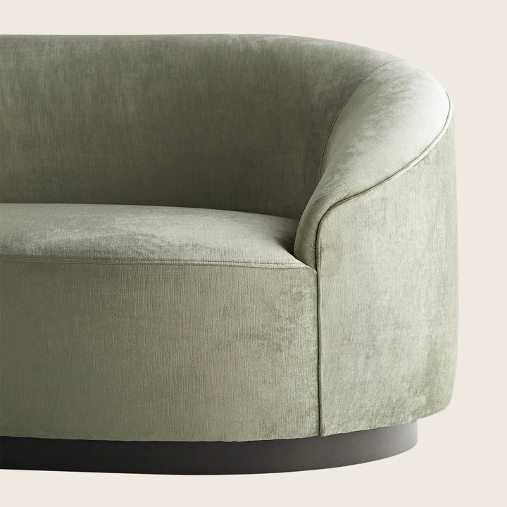 Close-up of a pale green, curved couch with plush cushions.