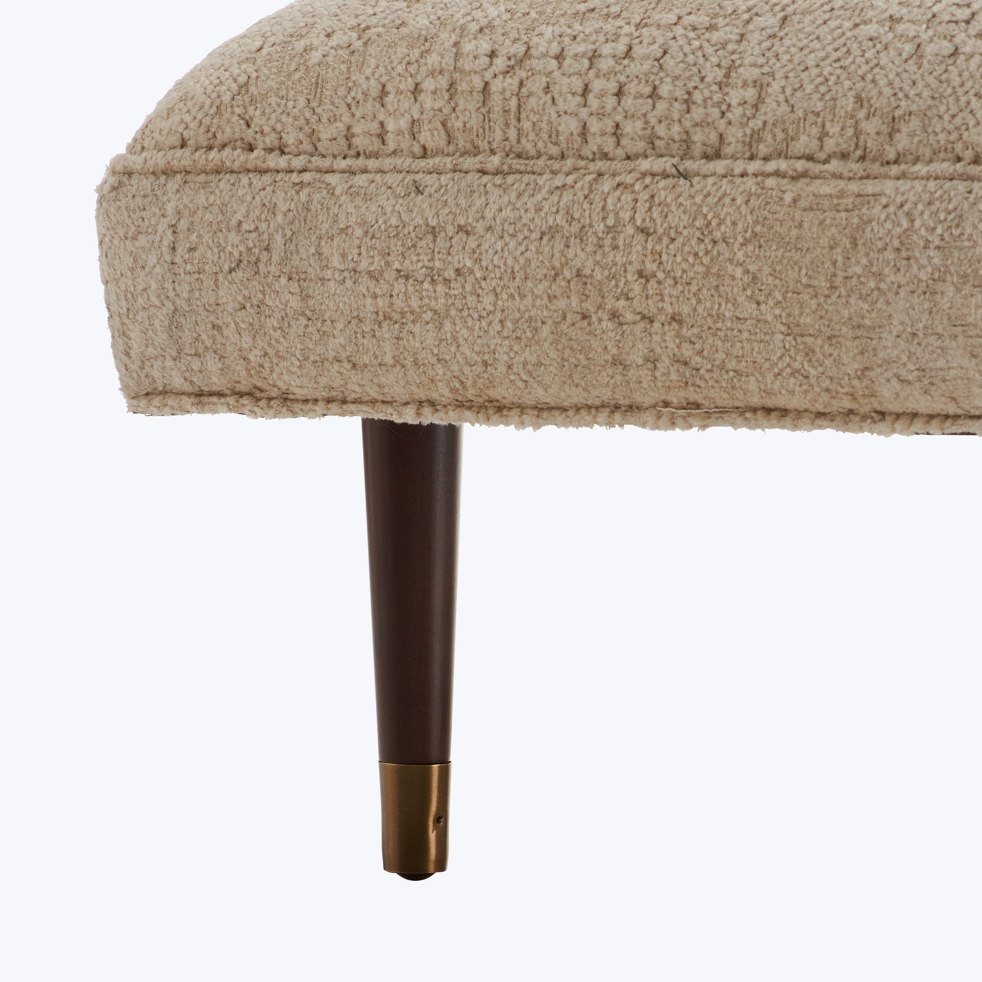 Close-up of a plush, beige sofa leg with dark wooden base and golden cap.