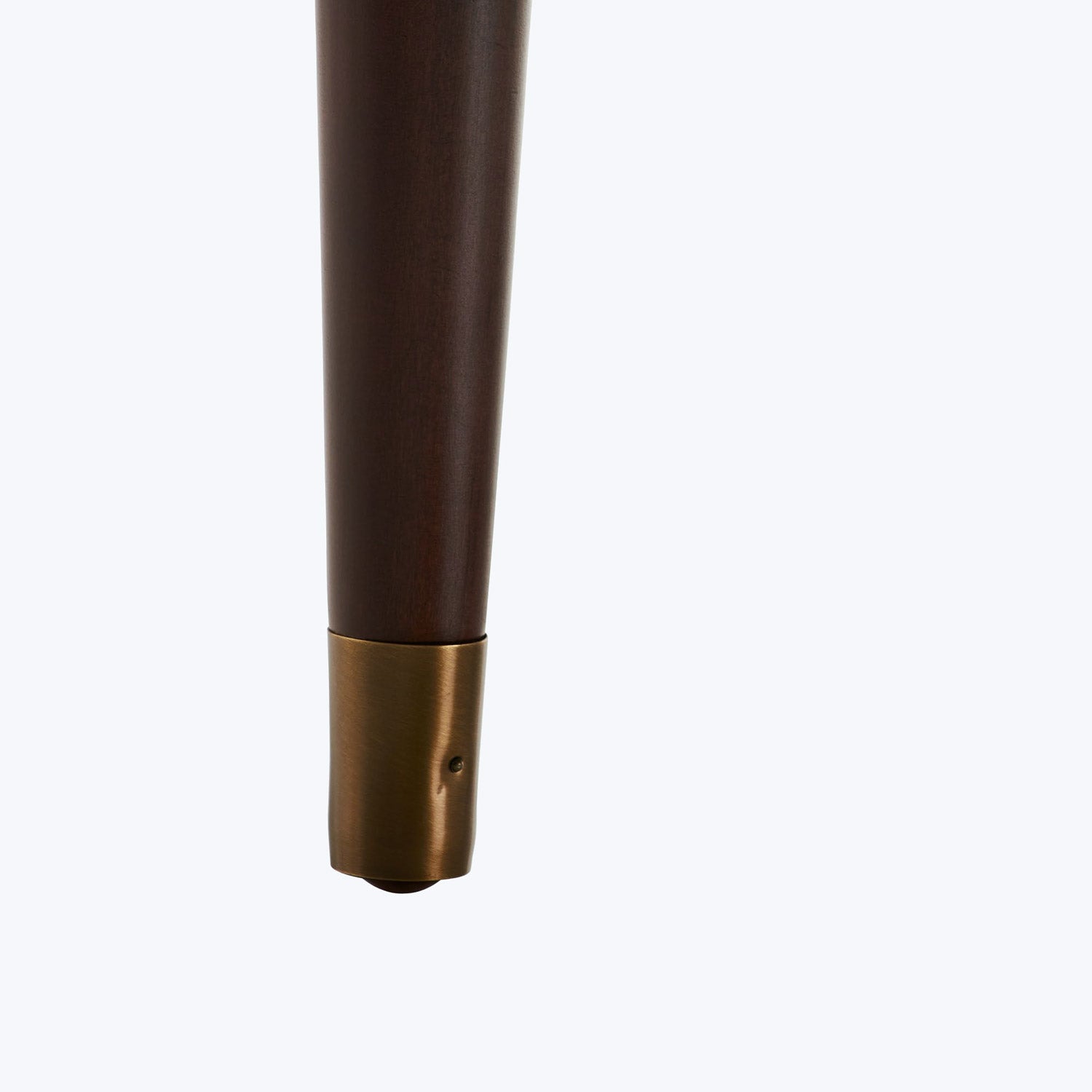 Close-up of a dark brown wooden table leg with brass cap.