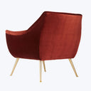 Modern armchair in burgundy velvet upholstery on gold metallic legs.