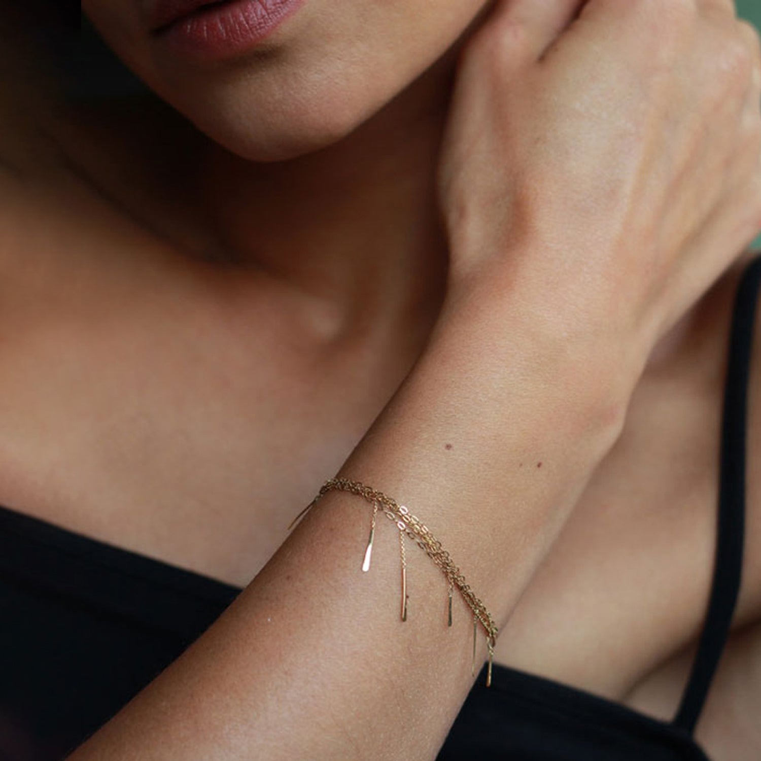 Close-up of person wearing gold-tone arm bracelet with dangling rods.