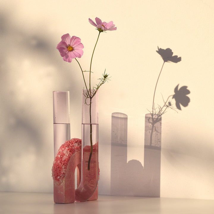 Still life with pink cosmos flowers and textured decoration piece.