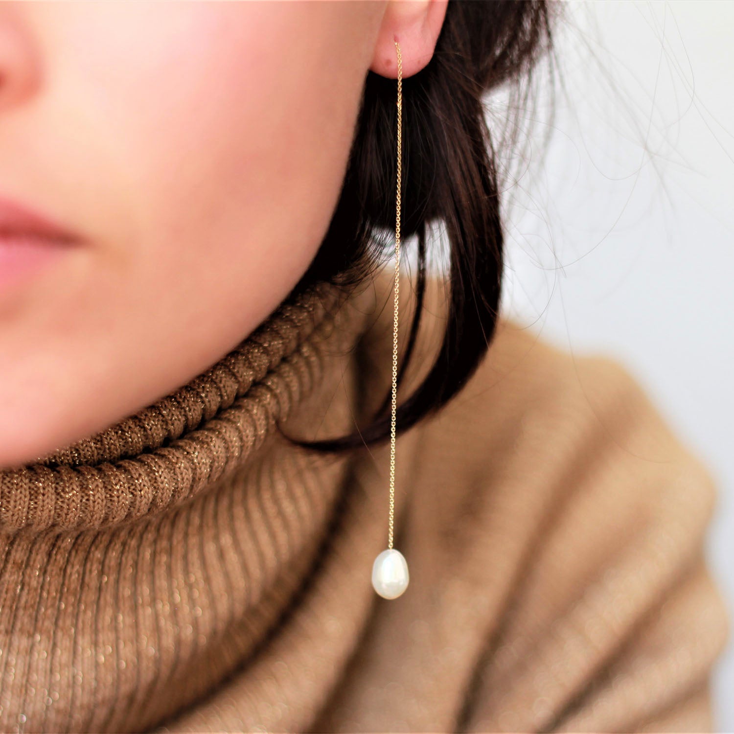 Close-up of person in brown turtleneck sweater wearing elegant earring.