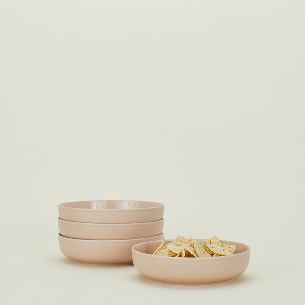A stack of light pink bowls with tortilla chips beside.