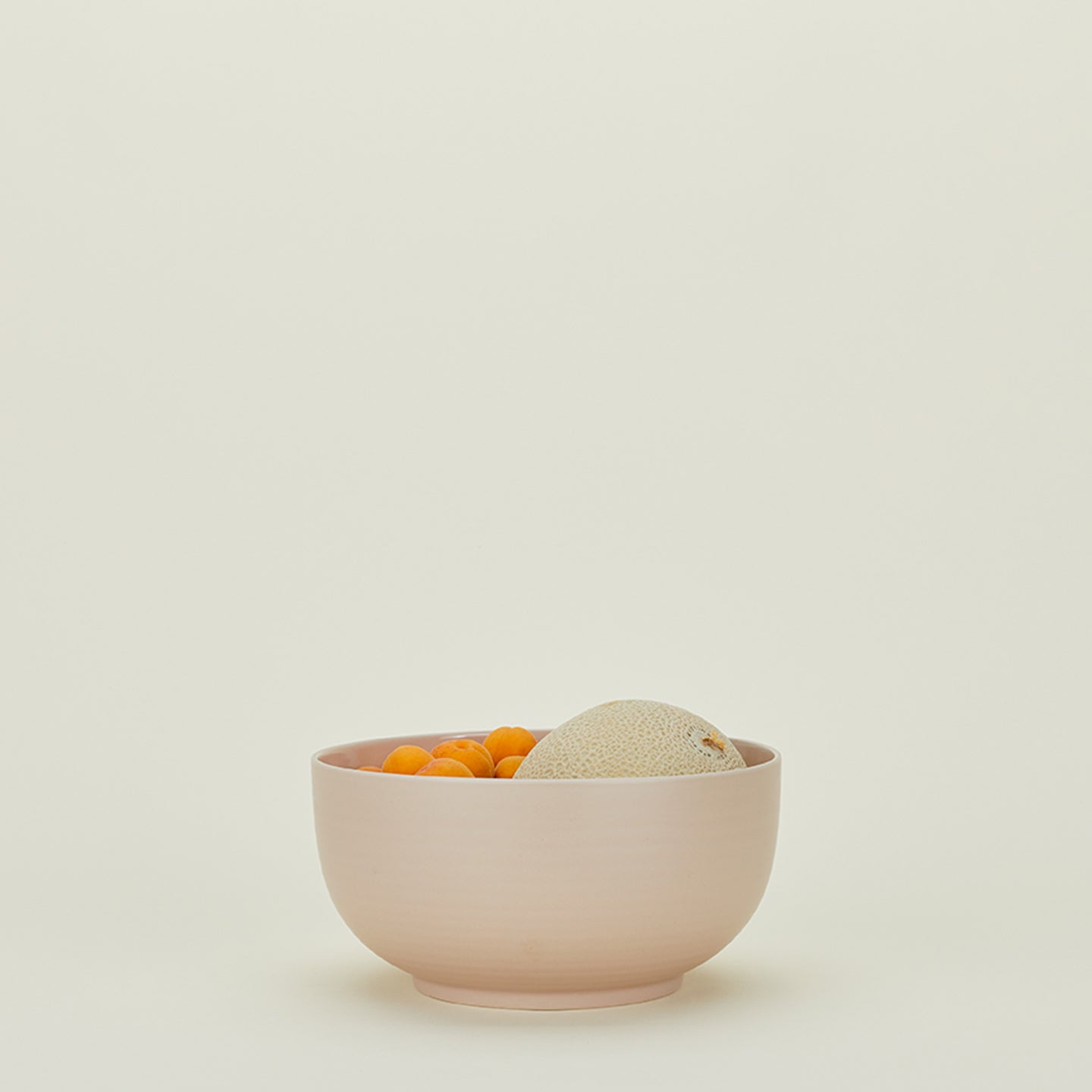 Minimalist still life featuring pink bowl with apricots and cantaloupe.