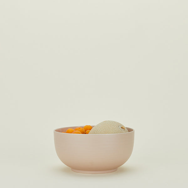 Minimalist still life featuring pink bowl with apricots and cantaloupe.