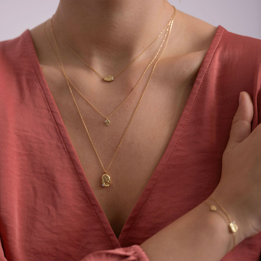 Modern and trendy gold jewelry layered on pink V-neck garment.