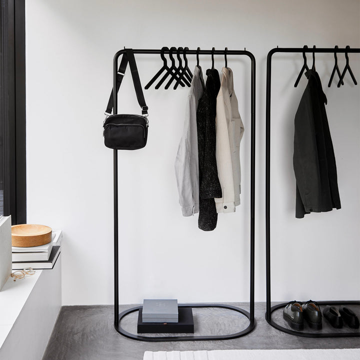 Minimalist black coat stand in white room with modern decor.