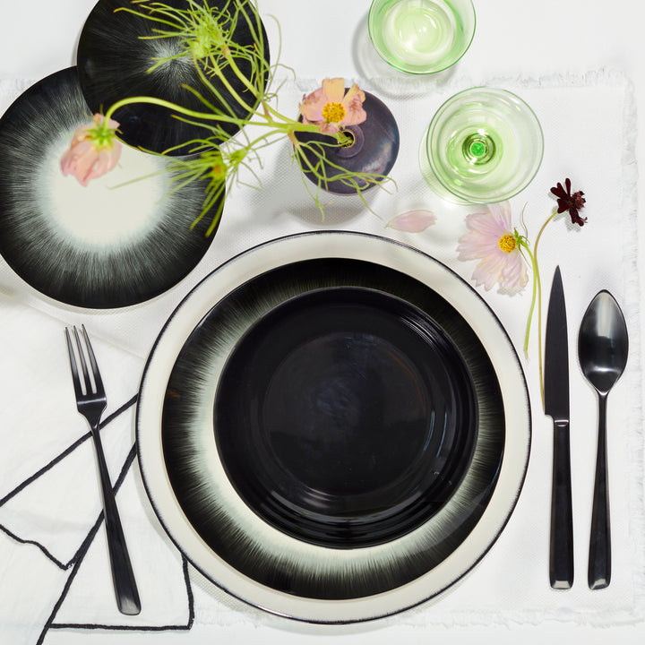 Elegant table setting featuring stacked plates, sleek cutlery, and delicate glassware adorned with flower blooms.