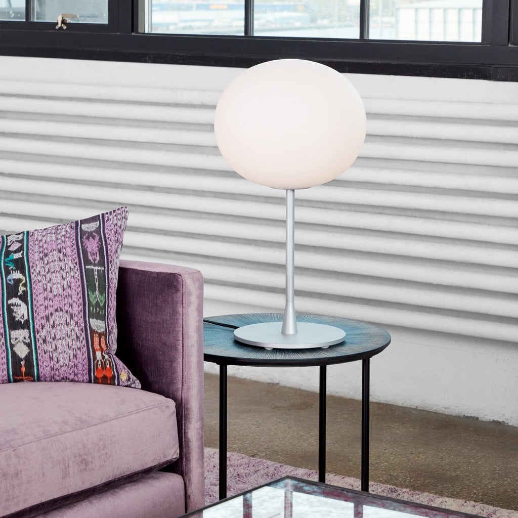 Minimalistic interior with a sleek lamp, textured side table, and colorful chair.
